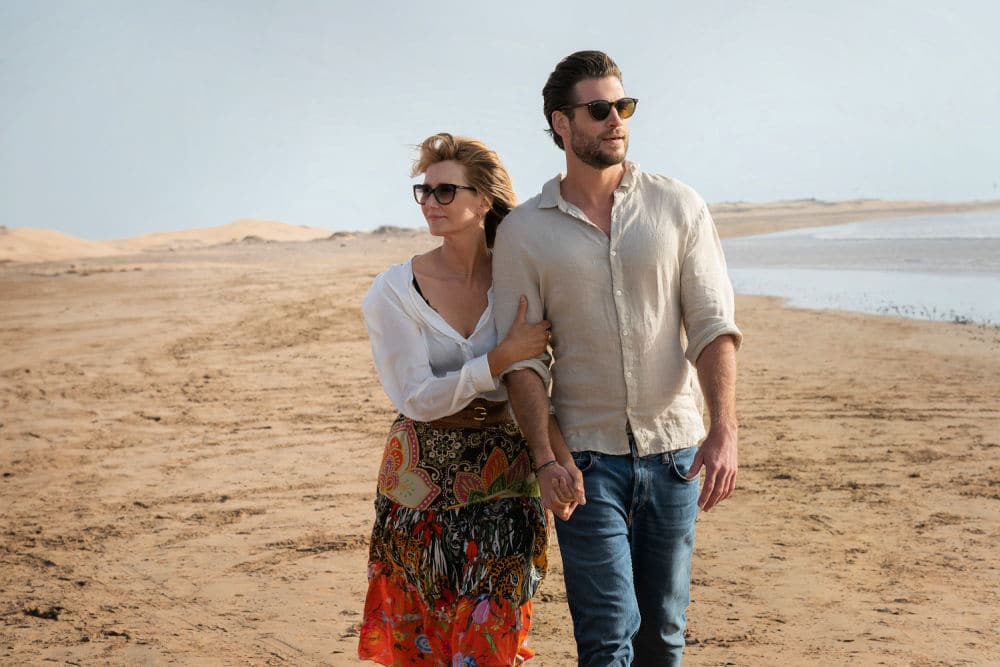 Laura Dern and Liam Hemsworth walking hand in hand along a serene beach, portraying their characters Katherine and Owen in a