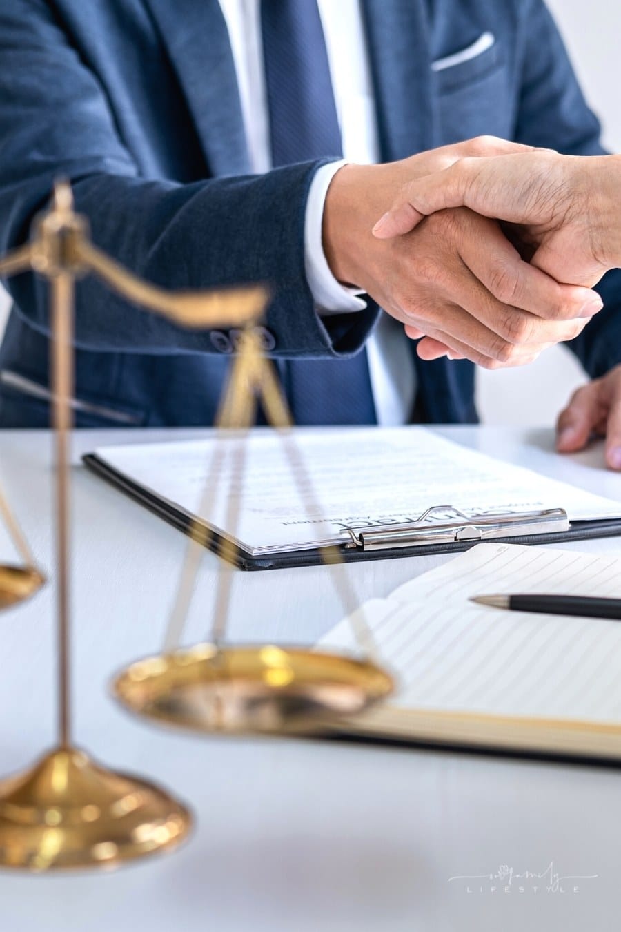 lawyer and client shaking hands behind legal scale and gavel