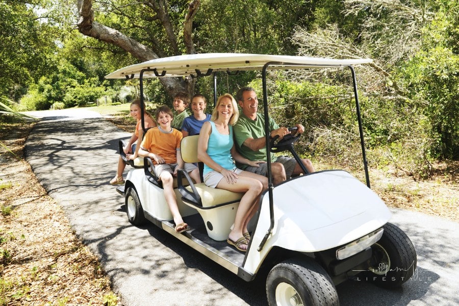 family riding on golf cart along tree-shadowed trail