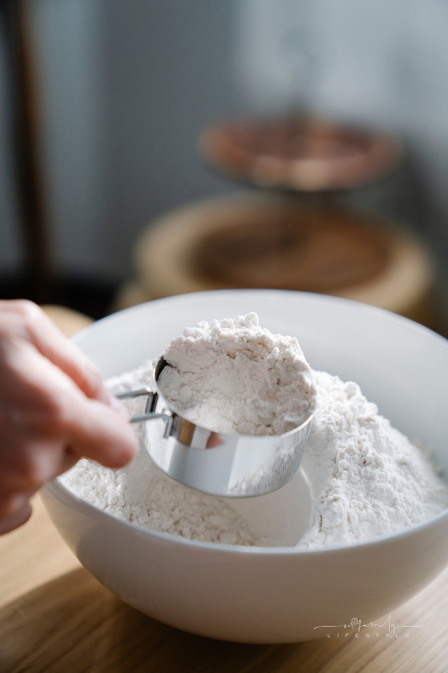 woman's hands measuring flour out of a bowl with a metal measuring cup