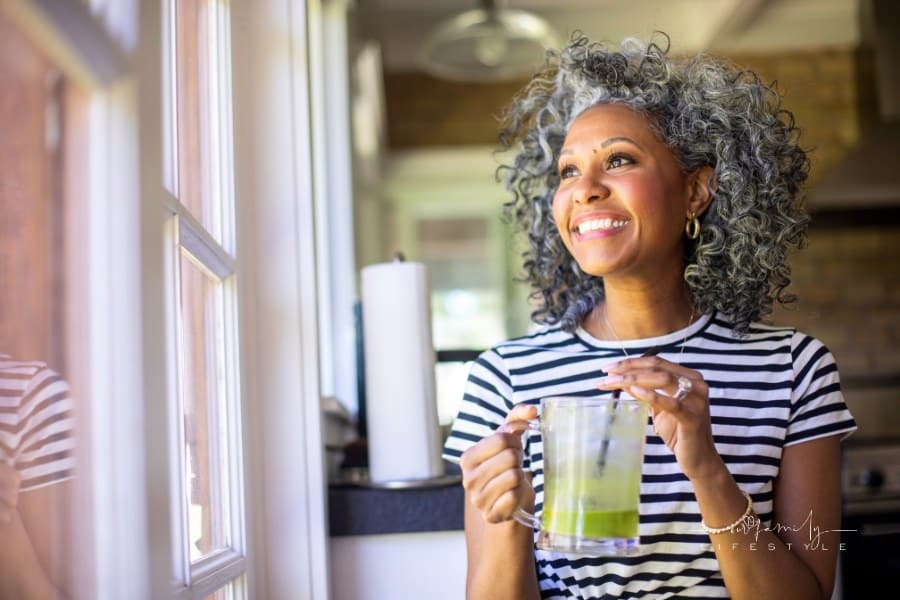 Middle-aged Black Woman with white curly hair Drinking a Green Smoothie in kitchen