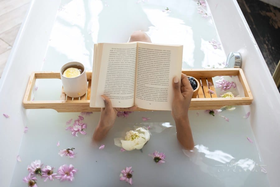 Woman reading book and drinking tea while resting in bathtub