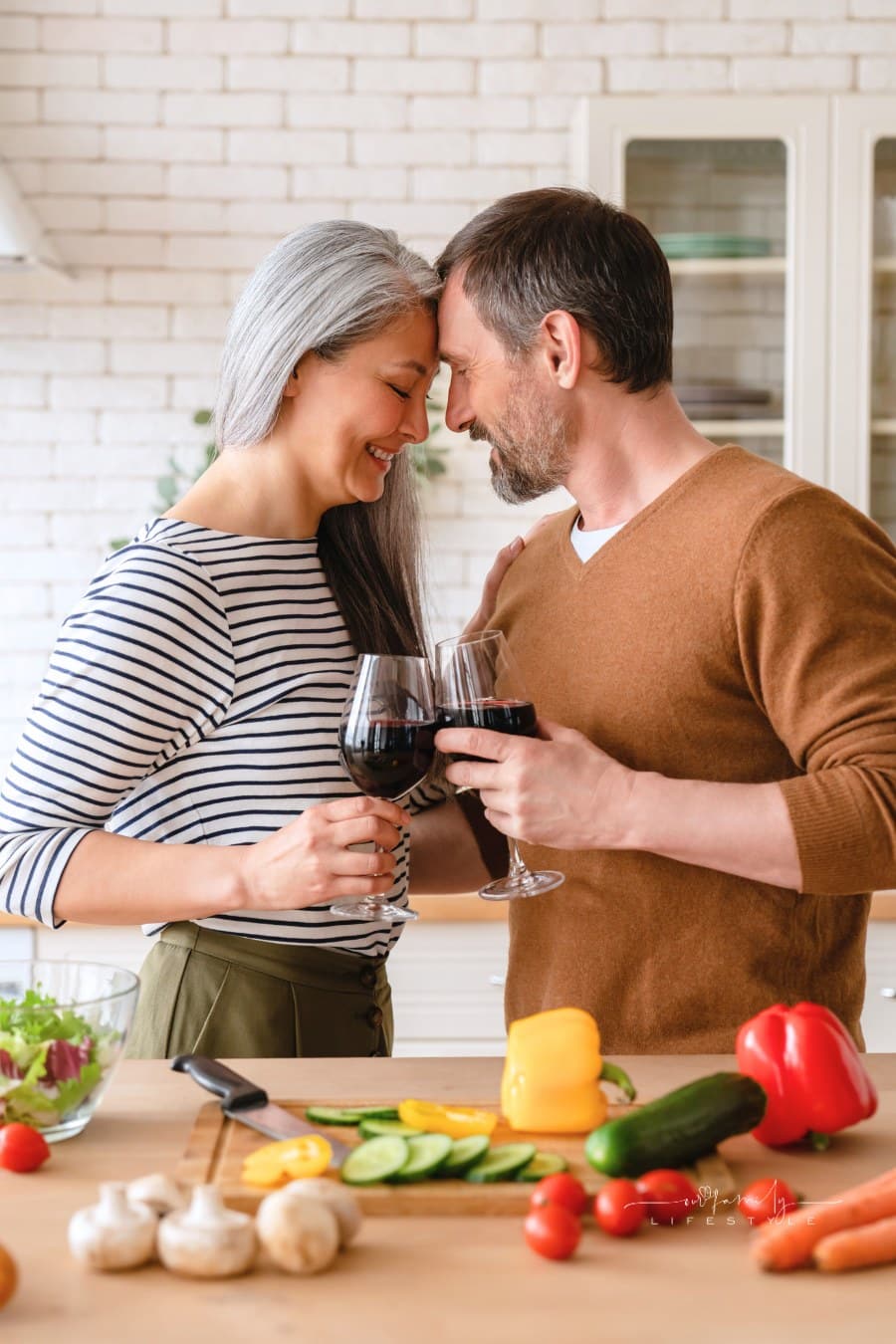 mature middle-aged couple drinking wine while cooking romantic dinner vegetable salad together in the kitchen at home.