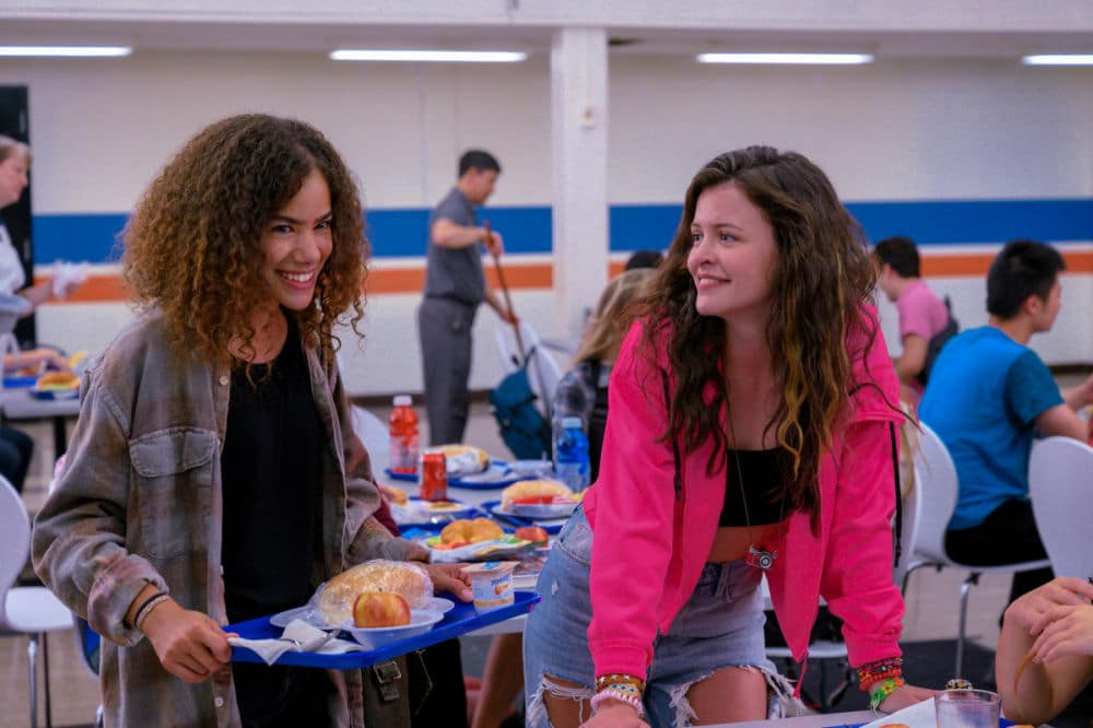 Scene from Netflix's series 'Ginny & Georgia,' featuring cast members Ginny and Maxine sharing a moment in the school cafeteria, highlighting their friendship dynamic.