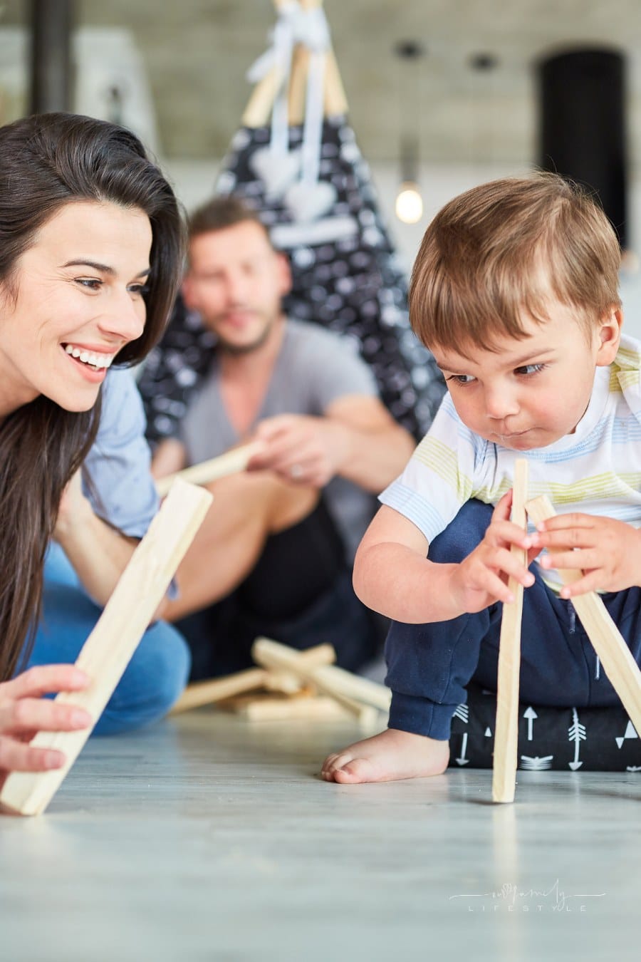 Mother helps child play camping and piling wood in the living room at home