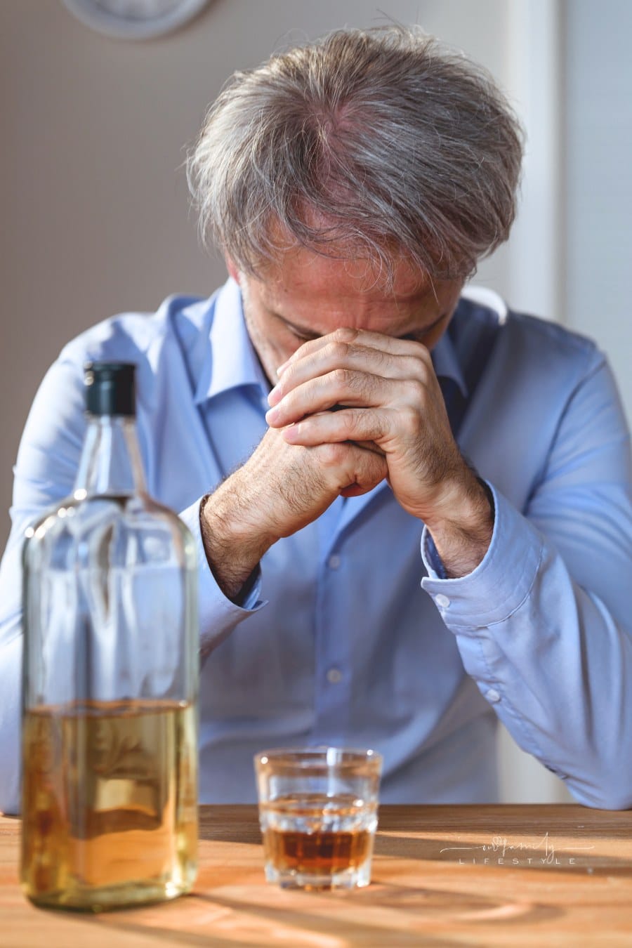 man drinking whiskey at table with head in hands