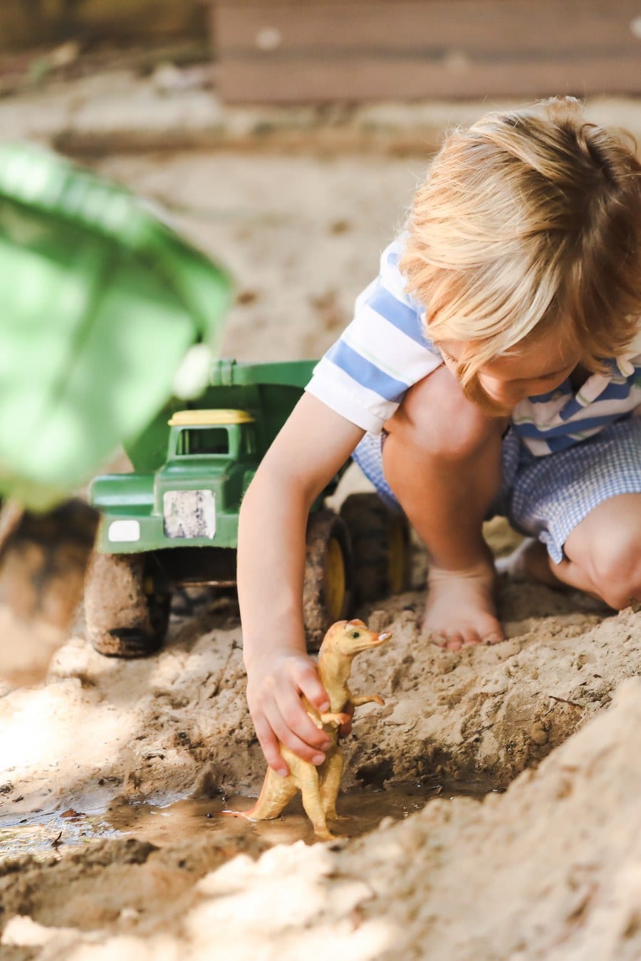 Preschool boy playing with diggers and trucks in sandpit