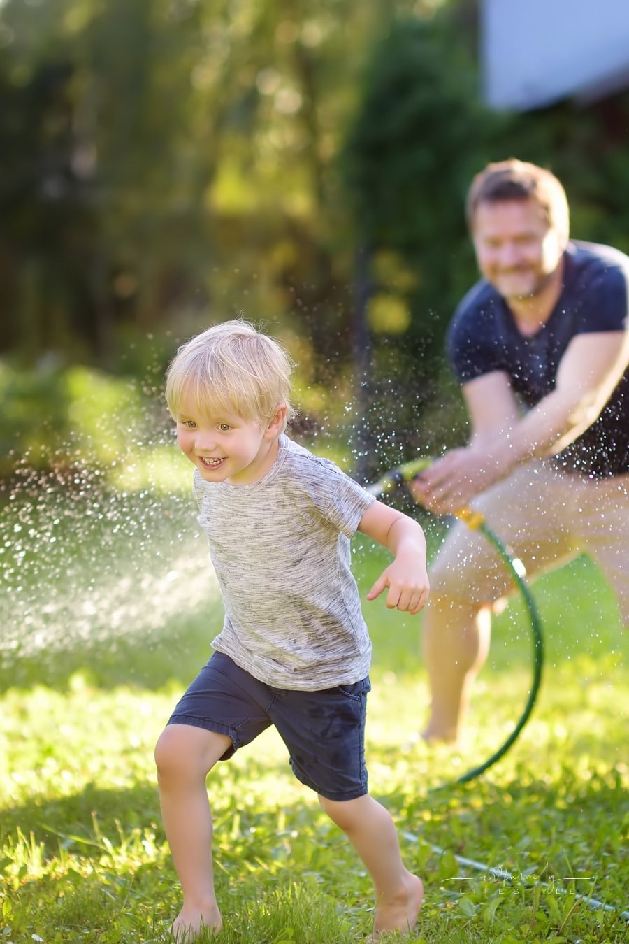 dad spraying son with water hose as they run through the yard