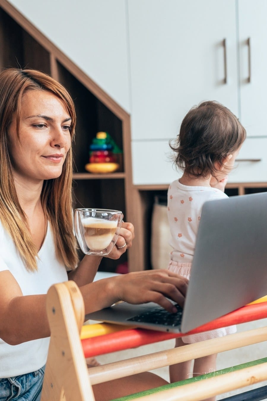 mom with wo small children working on laptop while they play nearby