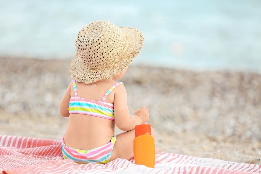 Baby Girl wearing sun hat with Sunscreen Cream on Beach