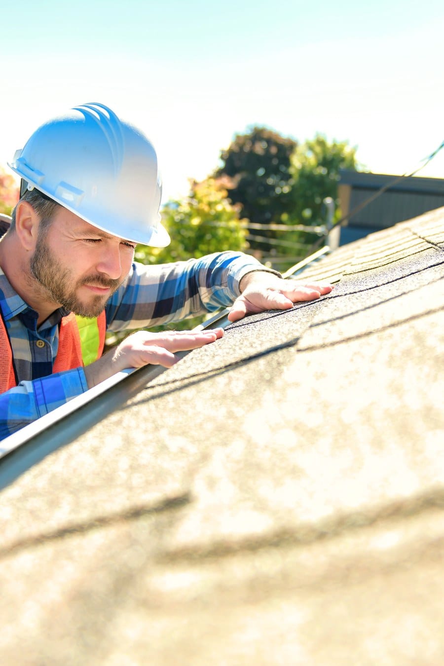 man with hard hat standing on steps inspecting house roof