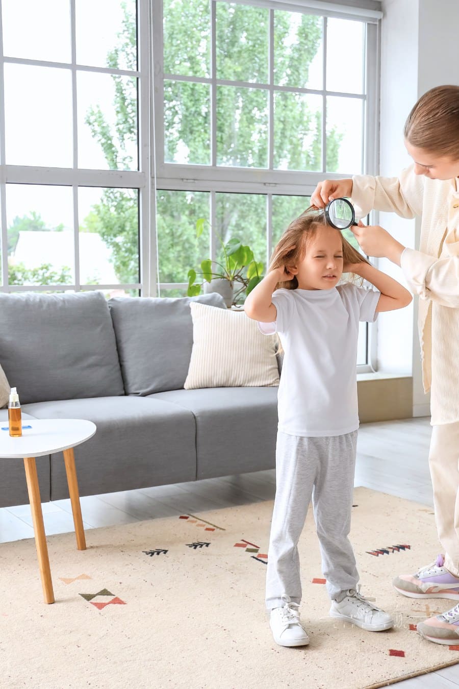 Mother with Magnifier Checking Her Little Daughter's Hair with Lice at Home