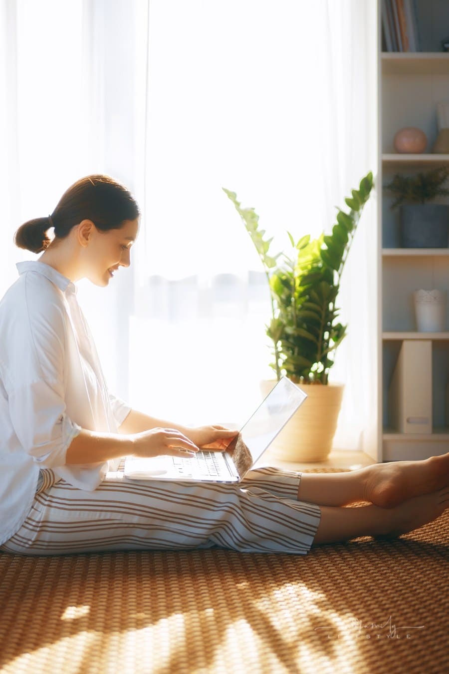 woman with laptop sitting on floor in front of large window