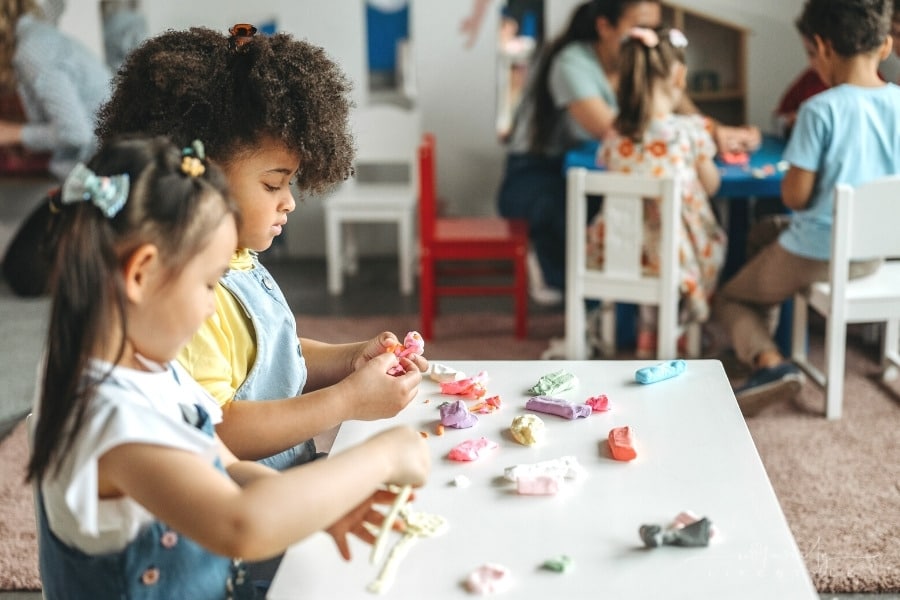 young girls sitting at a table working with clay in preschool setting