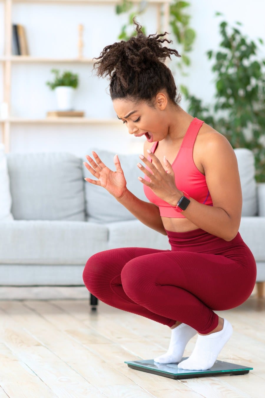 Happy Postpartum Woman Excited While Squatting On Weight-Scales Indoors
