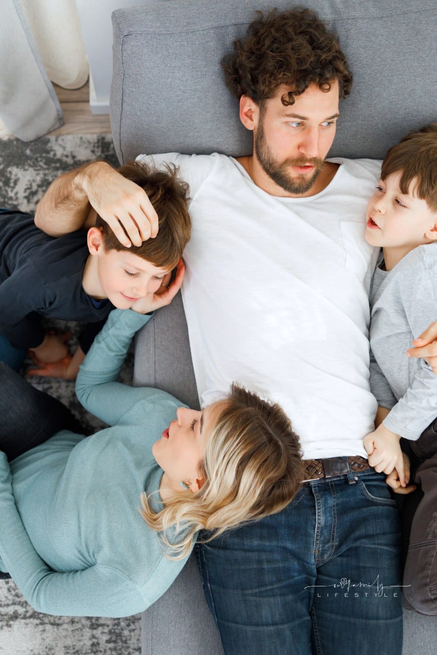 mom and dad lying on couch with young sons