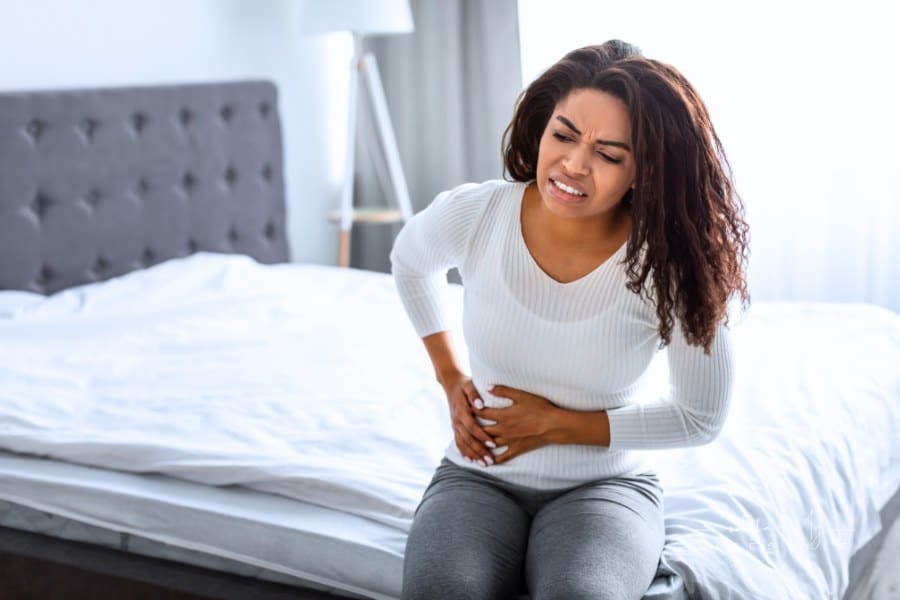 Woman with side pain sitting on bed at home