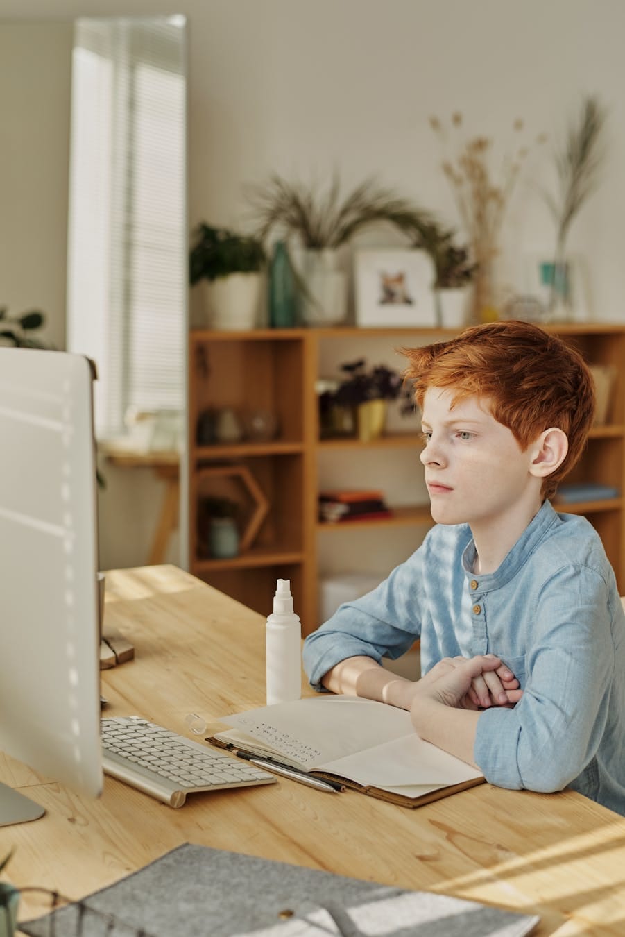 Red-haired boy focusing on online class at home during the day.
