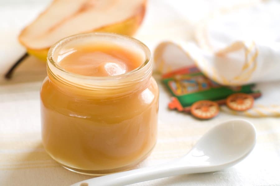 jar of baby food open sitting next to bib and pear