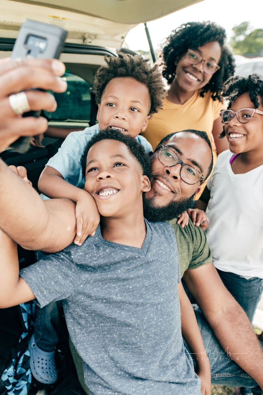 father with 4 kids taking a selfie in back of minivan before afmily road trip