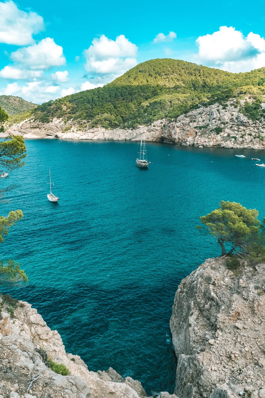 Sailboats drift in a stunning turquoise bay surrounded by rocky cliffs in Ibiza, Spain.