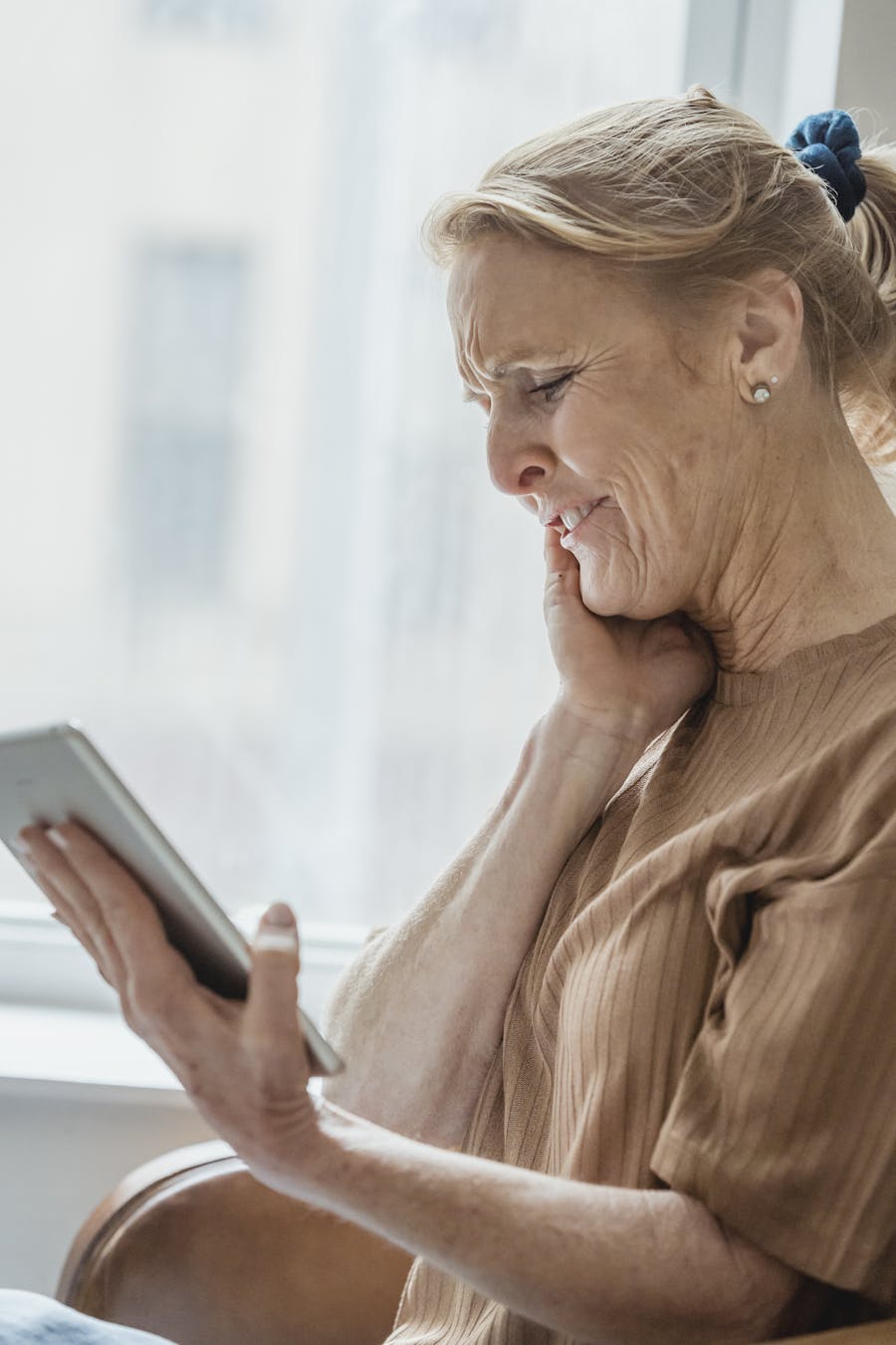 Senior woman smiling while using a digital tablet indoors with natural light.