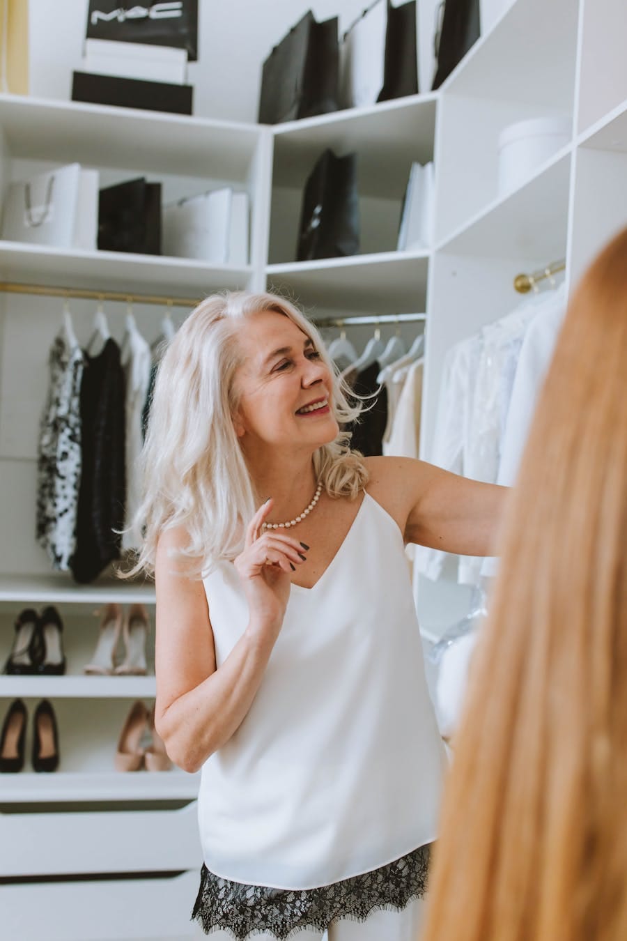Senior woman with white hair smiling while selecting clothes in a walk-in closet.