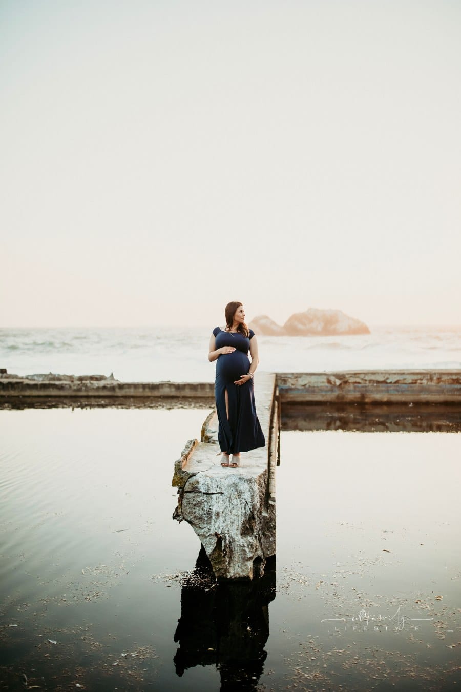 pregnant woman standing on concrete pier over ocean