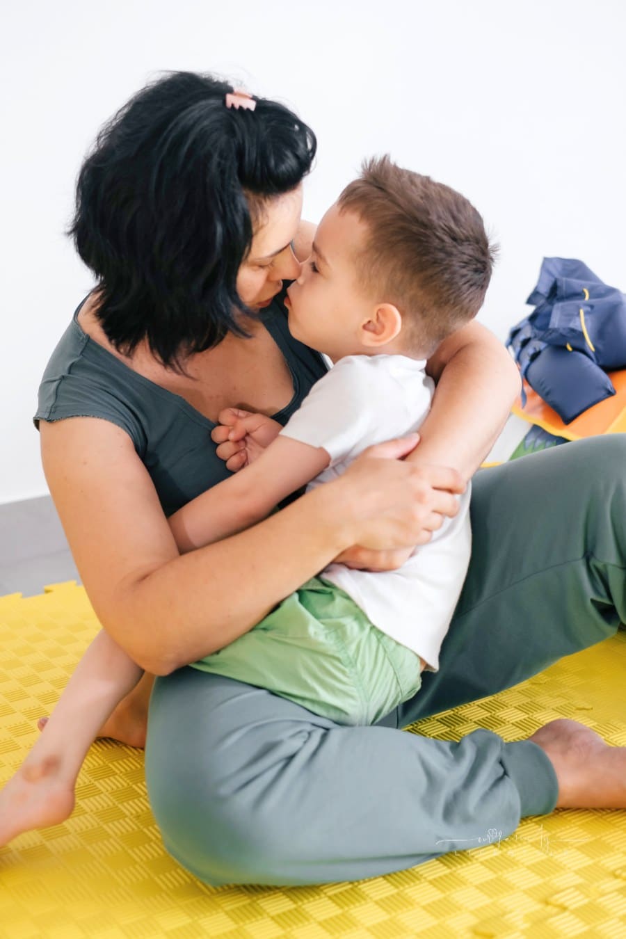 Mom holding happy son on the mat in child rehabilitation center. Boy with cerebral palsy smiling. Rehabilitation and inclusion kindergarten, day care. Disabled boy