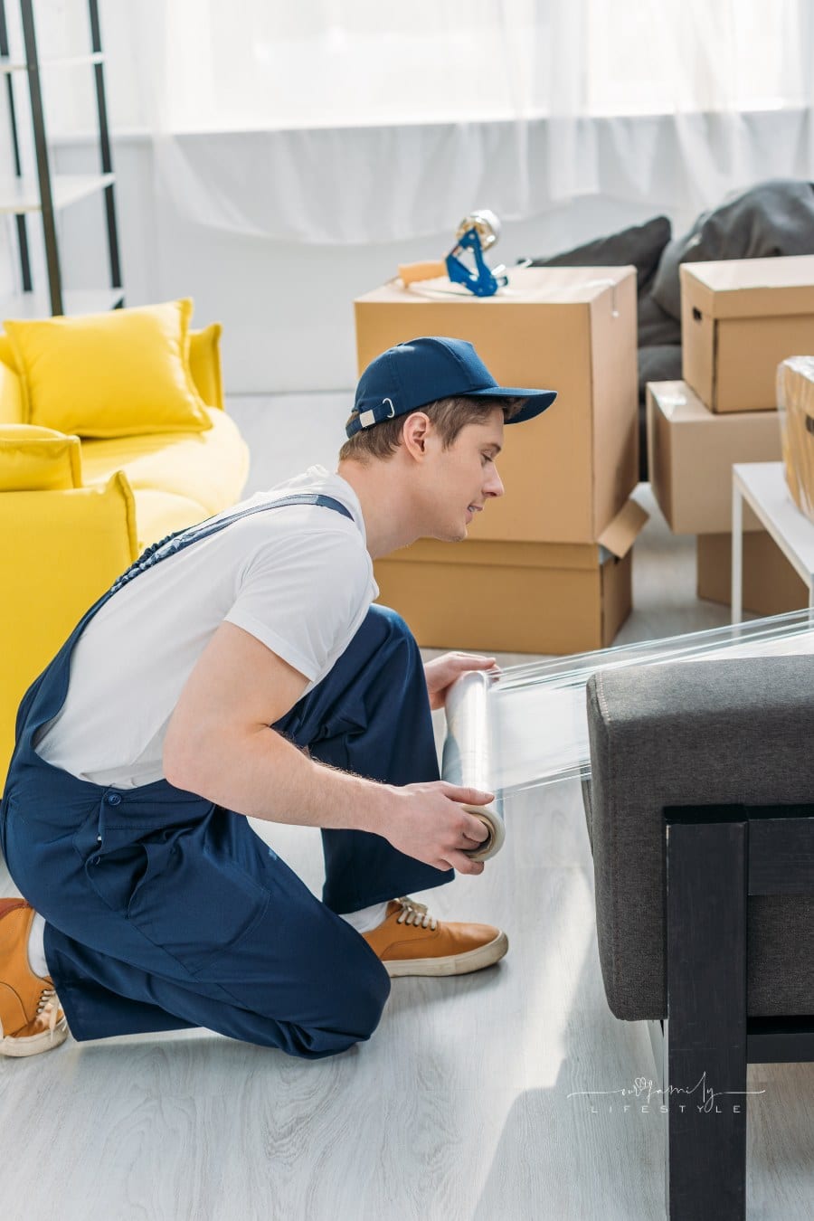 mover in uniform wrapping furniture with roll of stretch film in apartment
