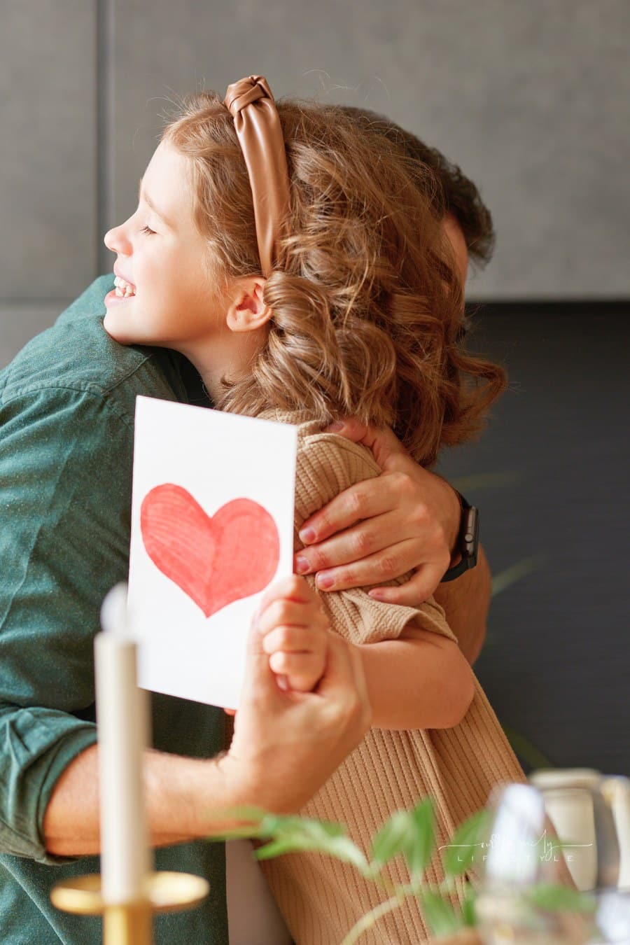 Happy dad getting hug from his cute daughter holding a handmade card with a heart