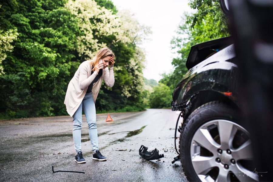frustrated woman talking on phone by damaged car after accident