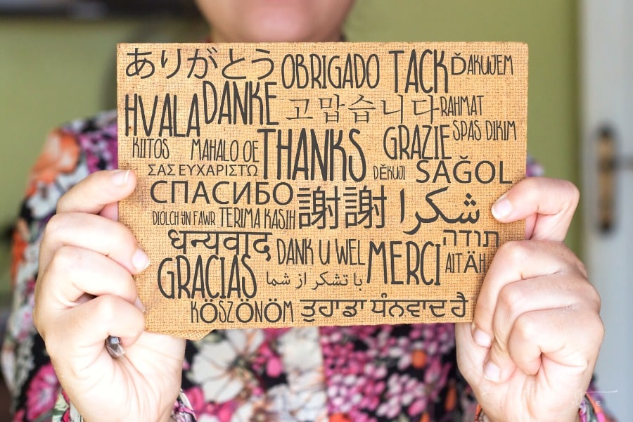 woman holding sign with thank you written in many different languages
