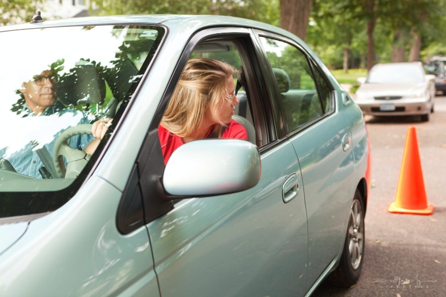 teen driver looking back at orange cone as father teachers her to parallel park