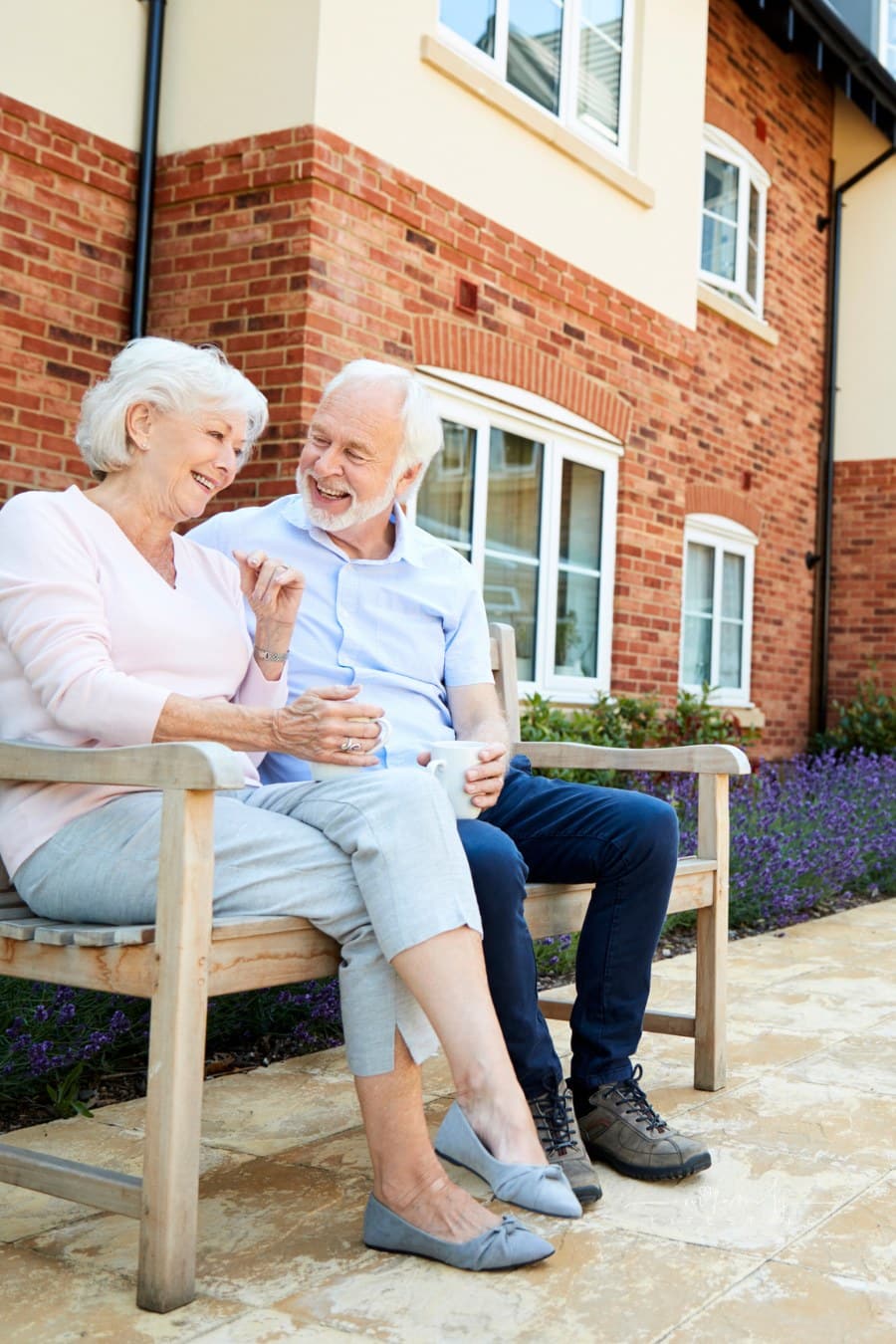Retired Couple Sitting on Bench with Hot Drink in Assisted Living Home