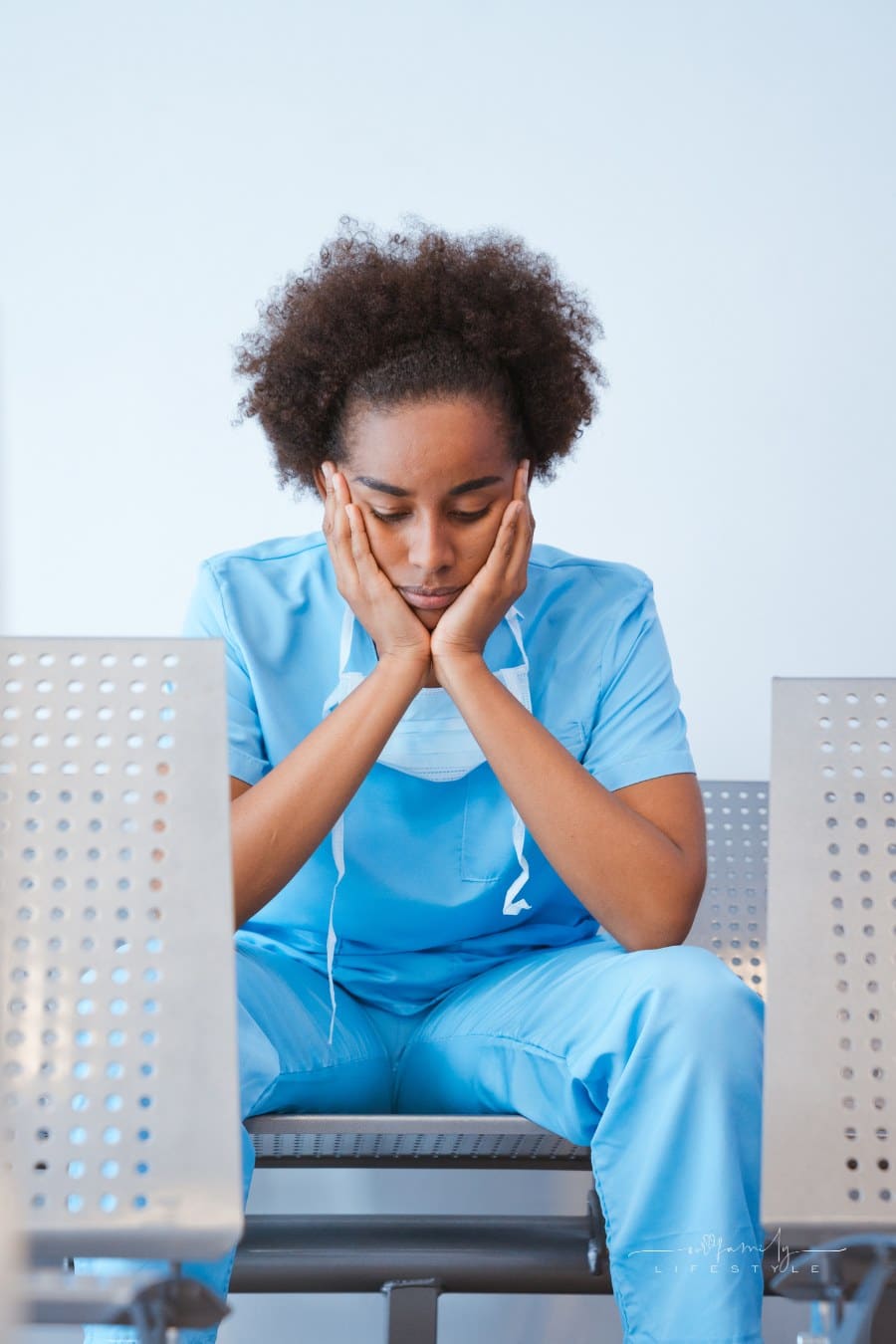 tired nurse sitting in waiting room chair with hands in head