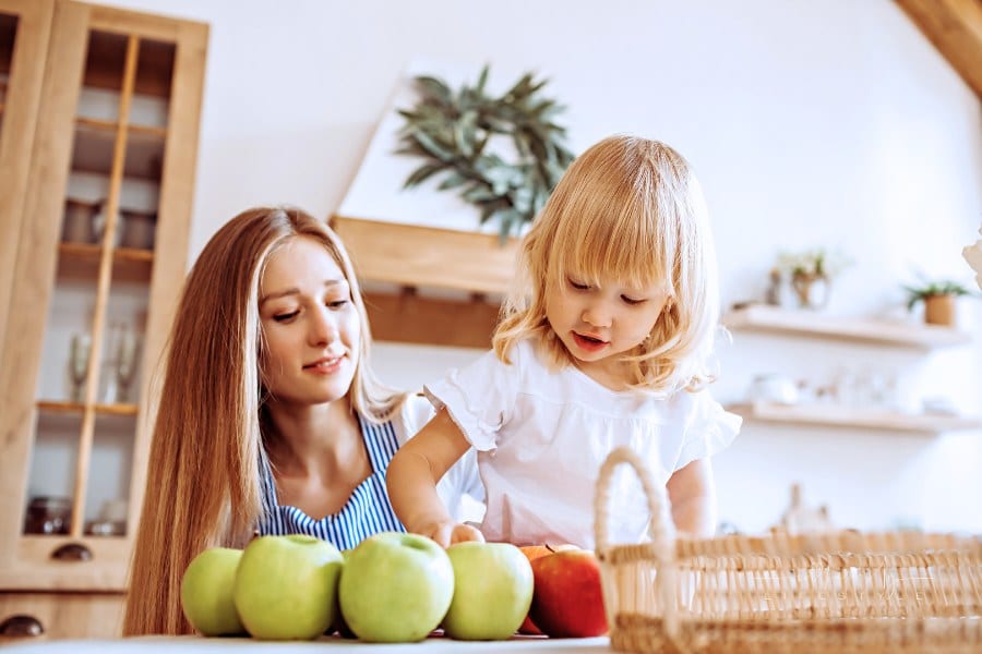 Little girl helps mom choose apples at the kitchen table