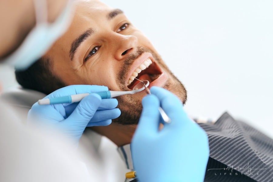 man with mouth open while dentist examines teeth with mirror
