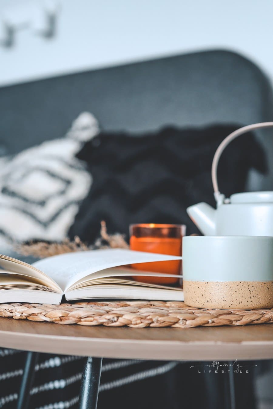 An open book, a cup of tea, a kettle and a candle on the background of the bed in the bedroom, home interior in fall