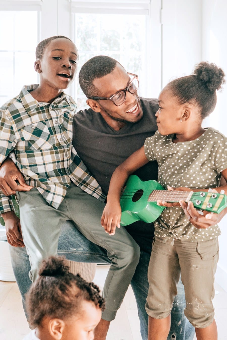 Dad is teaching kids new song on ukulele 
