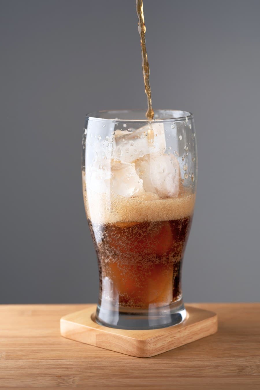 Soft drink with ice in glass on gray background.
