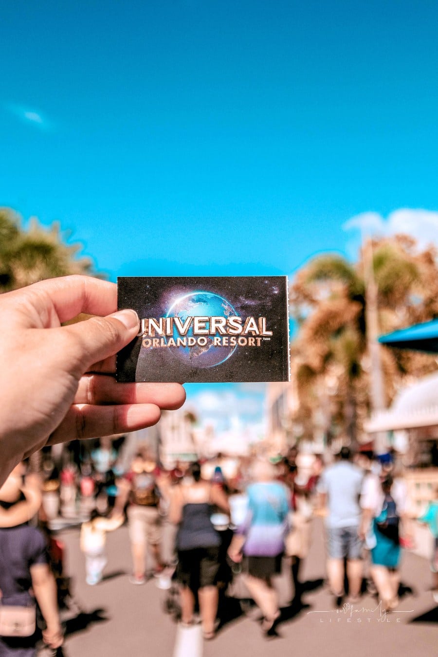 Person Holding Universal Studios Ticket in front of crowded theme park