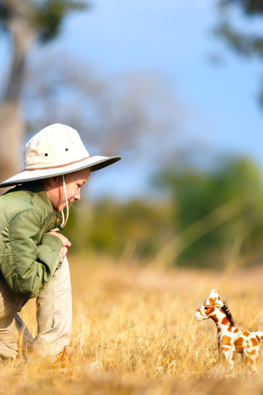 young girl bending down to smile at stuffed giraffe at safari park
