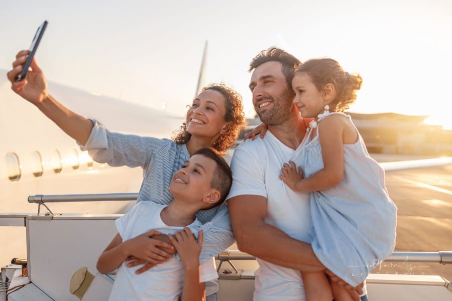 Happy family taking selfie while standing together outdoors ready for boarding the plane at sunset