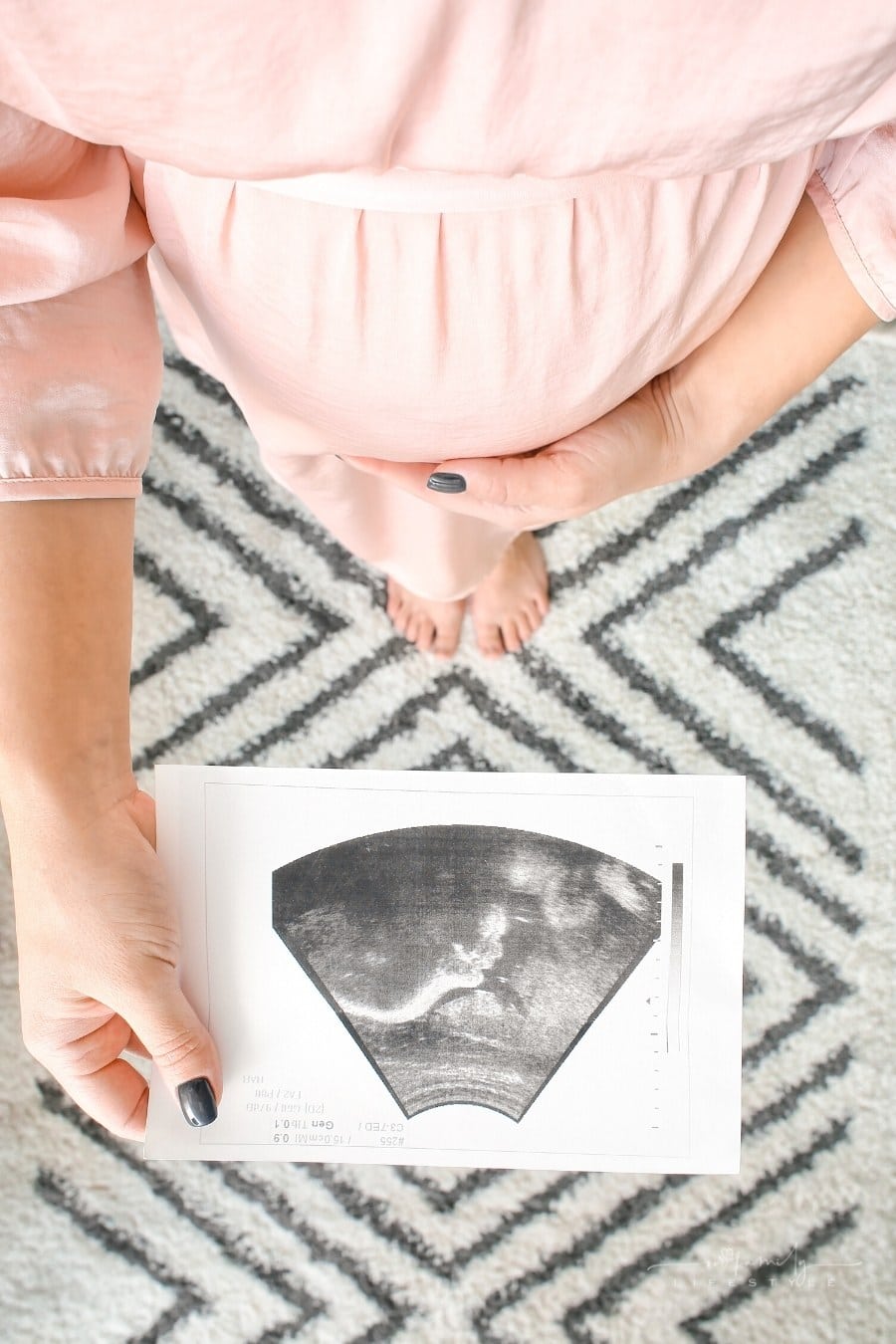 pregnant woman with one hand on stomach and other holding a sonogram