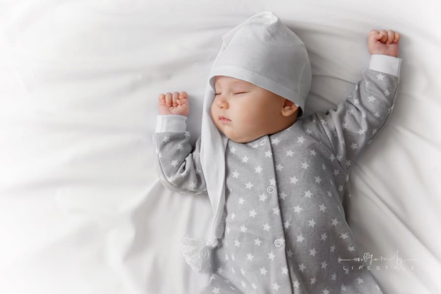 baby sleeping on sheet wearing pajamas and a night cap