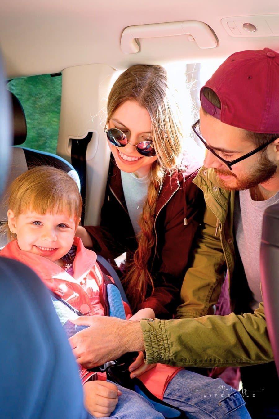 mother and father strapping young child into car seat