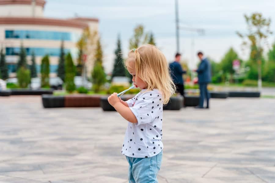 Little child girl eats fruit puree in pouch outside.