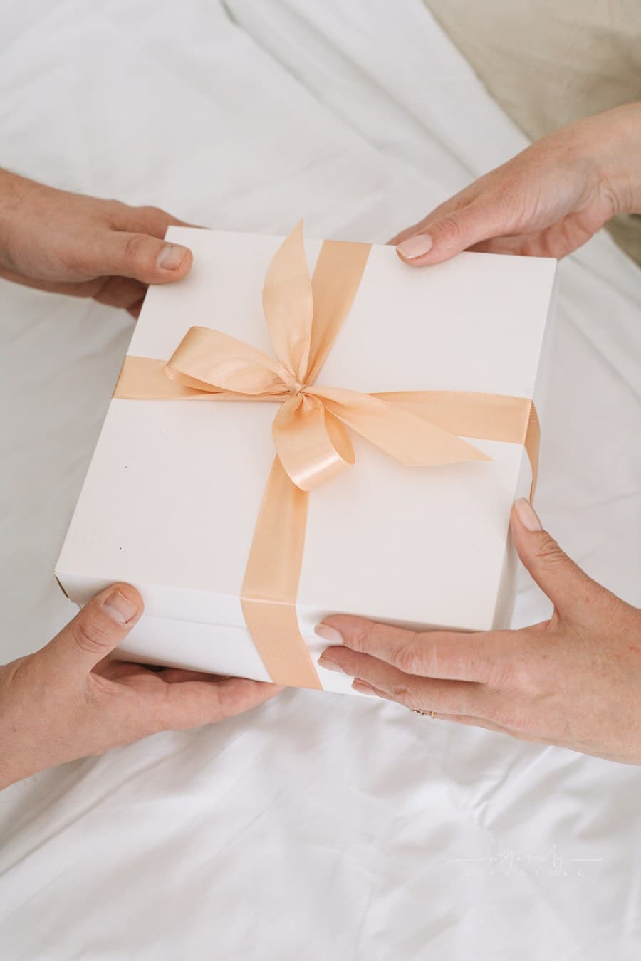 two sets of hands Holding Box with peach Ribbon