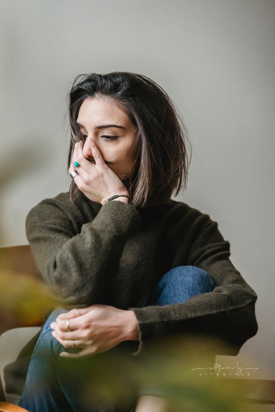 Unrecognizable upset woman embracing legs with other hand covering her face while sitting on chair